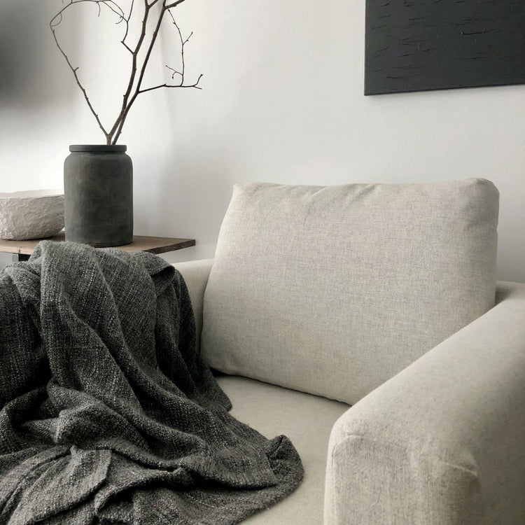 fauteuil avec un plaid, un édredon et un vase posé sur un meuble d'appoint